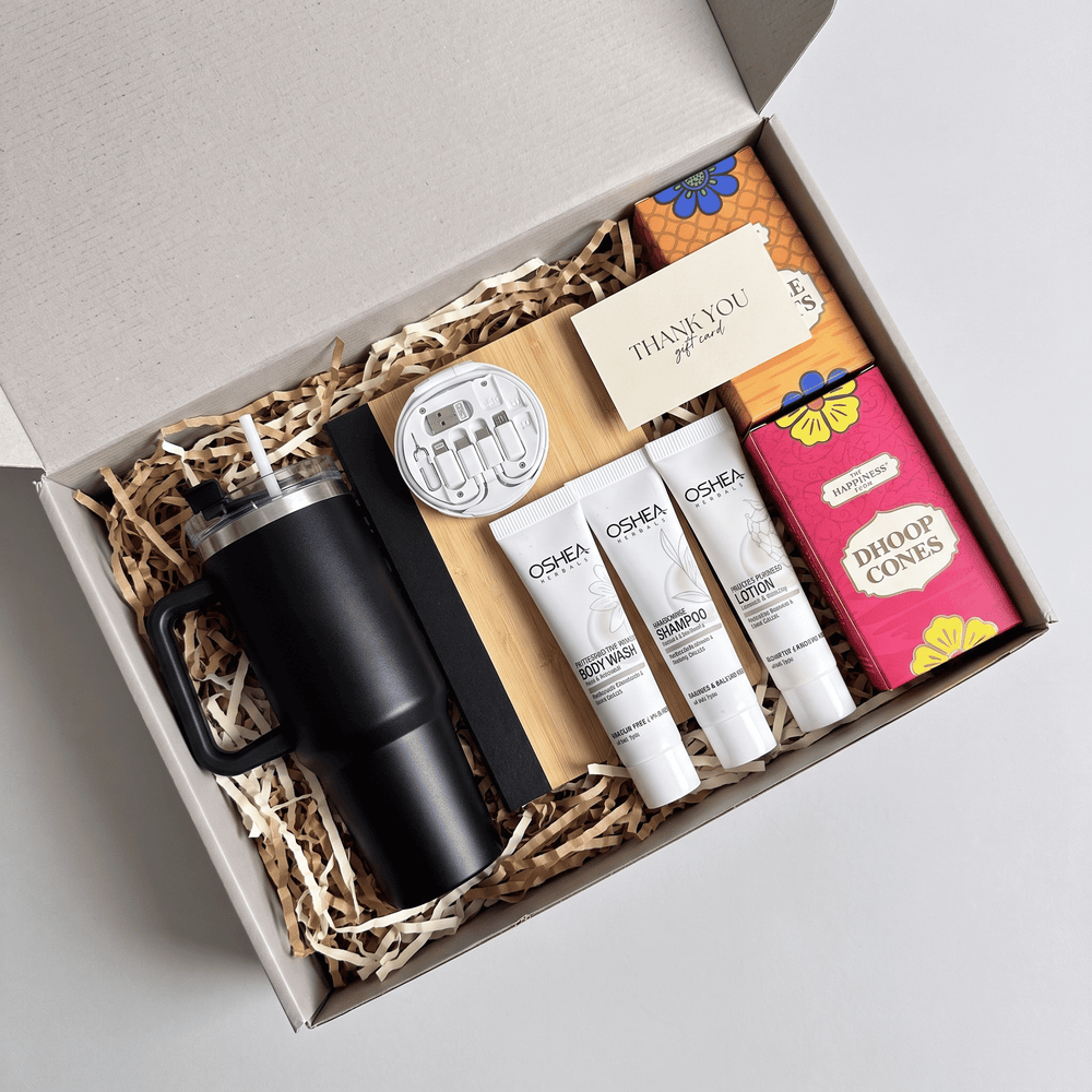 Everyday gift hamper open overhead: black travel tumbler, bamboo notebook, utility travel kit, three travel toiletries, chocolates and dhoop cones in a kraft gift box