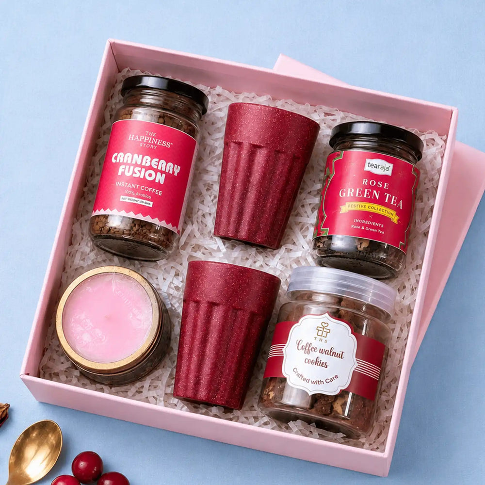Open pink gift box holding a jar of cranberry instant coffee, a jar of rose green tea, a jar of coffee walnut cookies, two deep red rice husk kullads and a lavender candle on white paper shred