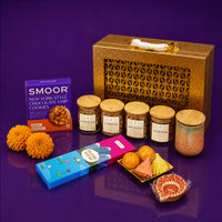 Gold Diwali gift case with its contents lined up beside it — labelled jars of chocolates, cashews, pistachios and almonds, a scented candle, incense sticks and modak and ladoo candles