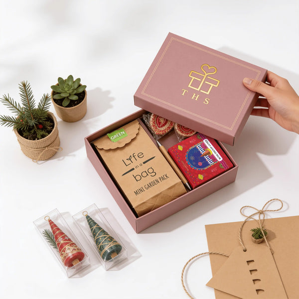 Hand lifting the lid of an eco-friendly Diwali gift box, showing a mini garden planter kit, a bamboo pen, a rose dhoop cones box and two hand-painted earthen diyas