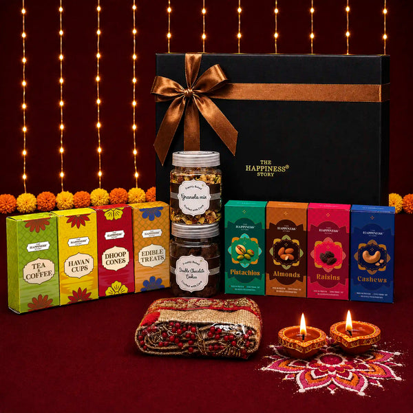 Premium black kappa board Diwali gift box with a bronze satin bow and gold foil logo, with granola, cookies, dry fruit cartons, tea, coffee, havan cups, dhoop cones and a jute toran arranged in front