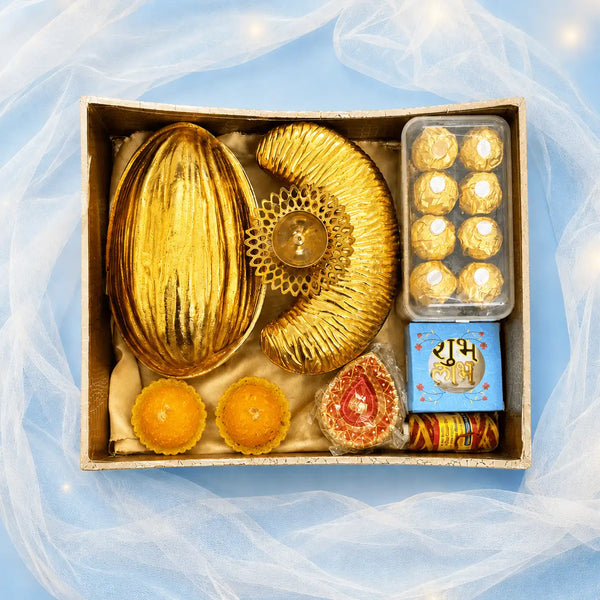 Top-down view of the packed luxury Diwali hamper — gold almond and cashew platters, a brass lotus diya, a tray of foil-wrapped chocolates, a Shubh Labh box, roli mouli, two ladoo candles and a hand-painted diya