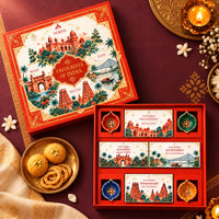Top view of the Favourites of India hamper with its illustrated lid, four snack boxes and four clay diyas; snacks on a brass plate styled beside it