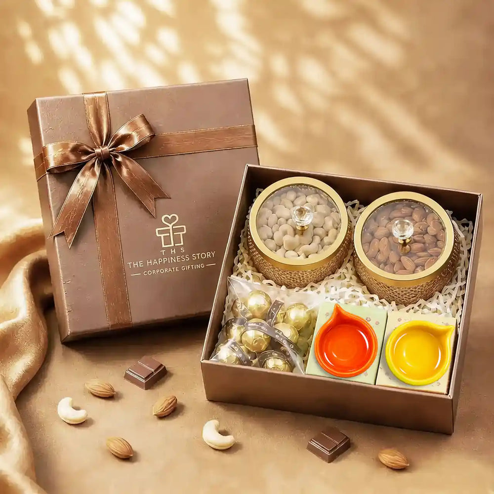 Diwali dry fruit gift hamper with almonds and cashews in gold glass-lidded jars, foil-wrapped chocolates and two ceramic diyas in an open brown gift box