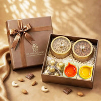 Diwali dry fruit gift hamper with almonds and cashews in gold glass-lidded jars, foil-wrapped chocolates and two ceramic diyas in an open brown gift box