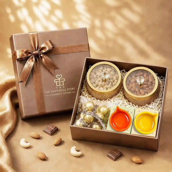 Diwali dry fruit gift hamper with almonds and cashews in gold glass-lidded jars, foil-wrapped chocolates and two ceramic diyas in an open brown gift box