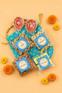 Diwali potli hamper contents laid out: 50g each of almonds, cashews and pistachios, a pack of chocolates and two hand-painted diyas on a turquoise sequinned potli