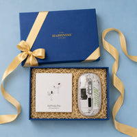Open navy blue gift box with a gold foil logo and gold ribbon, holding a sealed pair of Apple AirPods Pro and a transparent wireless mouse on kraft paper shred