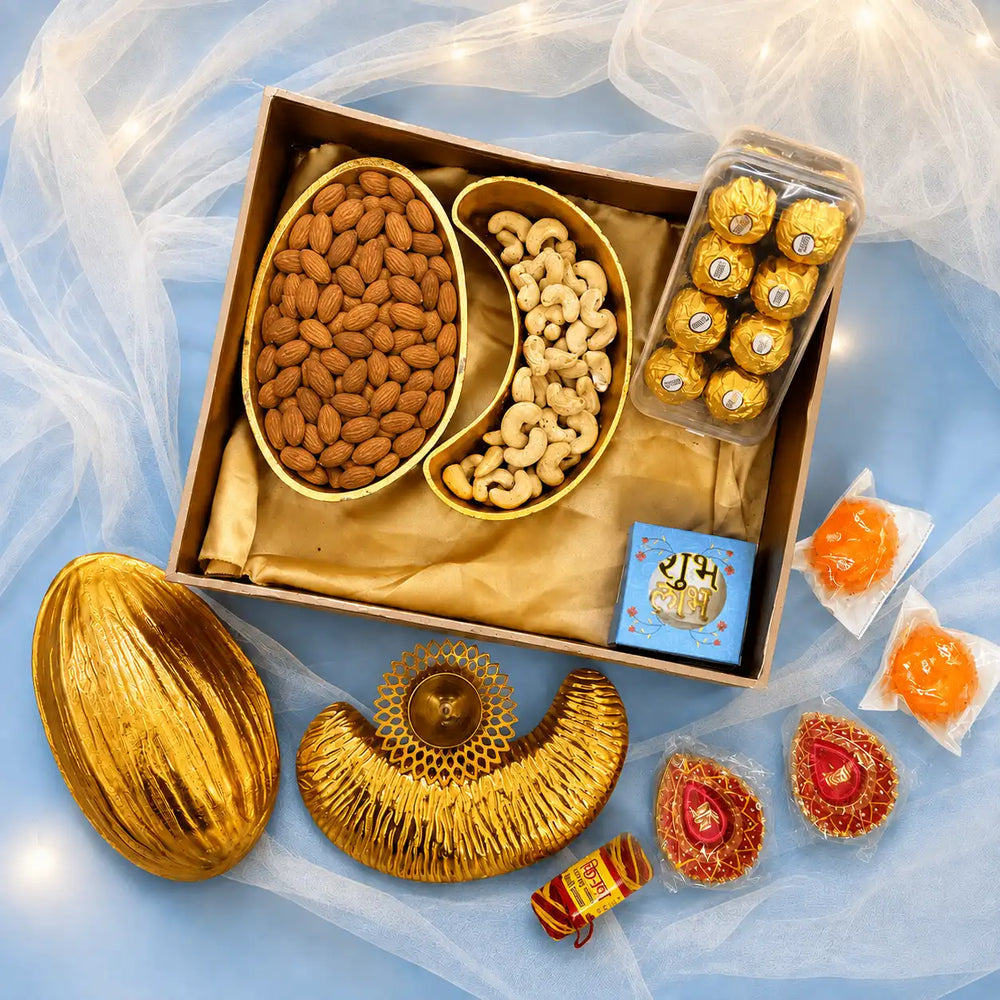 Luxury Diwali gift box with an almond-shaped gold platter of almonds and a cashew-shaped gold platter of cashews, beside a second pair of empty platters, a brass diya, painted diyas, ladoo candles, roli mouli, chocolates and a Shubh Labh