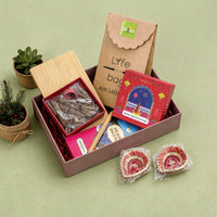 Rose dhoop cones box open with its sliding bamboo lid and terracotta cone holder, beside an incense sticks carton, a bamboo pen, a mini planter kit and two hand-painted earthen diyas