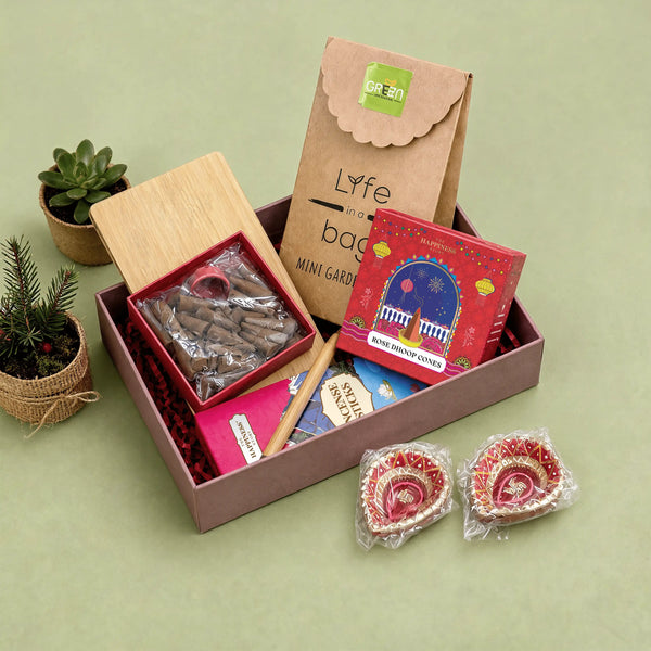 Rose dhoop cones box open with its sliding bamboo lid and terracotta cone holder, beside an incense sticks carton, a bamboo pen, a mini planter kit and two hand-painted earthen diyas