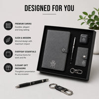 Canvas Core executive gift set styled on desk — grey canvas notebook, pen, earbuds case, snap-tab card holder and keychain with black packaging