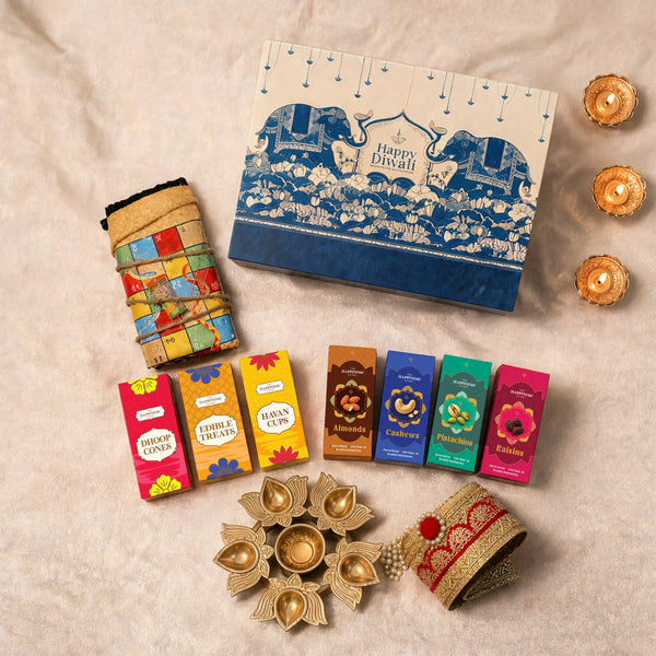 Overhead flat-lay of the eco-friendly Diwali hamper with the elephant-print gift box, rolled jute ludo board, seven printed cartons, five-well lotus urli, gold-zari jute toran and three lit diyas