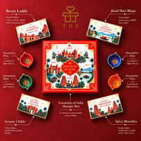 Labelled contents of the Favourites of India hamper: besan laddu, jhal muri, chikki, murukku and four painted diyas arranged around the red gift box