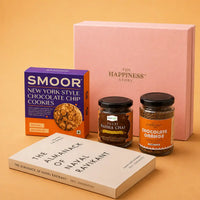 The Almanack of Naval Ravikant paperback laid flat in front of a jar of tulsi kadha chai, a jar of chocolate orange instant coffee, a cookie carton and a closed pink gift box