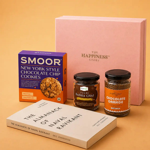 The Almanack of Naval Ravikant paperback laid flat in front of a jar of tulsi kadha chai, a jar of chocolate orange instant coffee, a cookie carton and a closed pink gift box