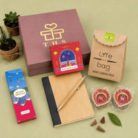 Eco-friendly Diwali gift hamper contents — bamboo notebook and bamboo pen, rose dhoop cones box, incense sticks box, mini planter grow kit and two hand-painted earthen diyas beside a dusty rose gift box