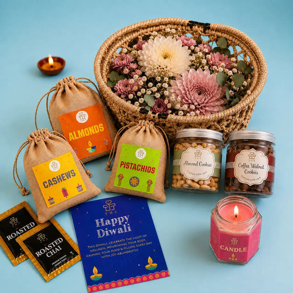 Diwali gift basket contents with the jasmine candle lit in its hexagonal glass jar, beside jute potlis of dry fruits, two cookie jars, roasted chai sachets and a Happy Diwali card