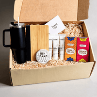 Angled view of the open everyday gift hamper with the lid raised and a gift card standing among the contents