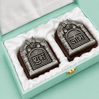 Open mint green gift box lined with white satin, holding the Shubh and Labh plaques seated in fitted wells, with a gold metal clasp at the front