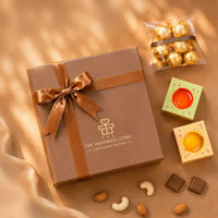 Overhead flat-lay of the closed brown ribboned Diwali gift box with foil chocolates and two ceramic diyas in printed cartons alongside