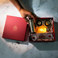 Overhead view of the opened Diwali hamper box with the coffee filter in hand and the star-filament bulb lit inside the tray