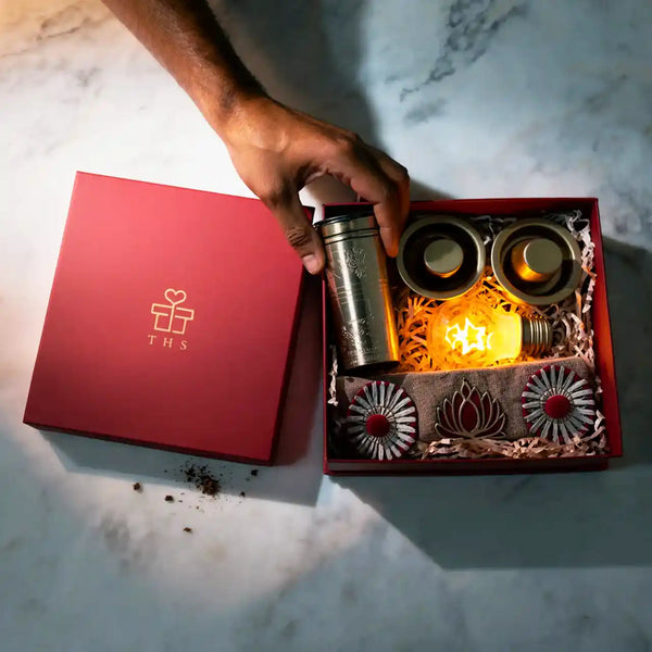 Overhead view of the opened Diwali hamper box with the coffee filter in hand and the star-filament bulb lit inside the tray