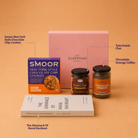 Labelled contents of the book and coffee gift hamper — New York style chocolate chip cookies, tulsi kadha chai, chocolate orange coffee and The Almanack of Naval Ravikant, standing in front of the closed pink gift box