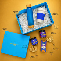 Labelled contents of the Diwali tea hamper — premium gift box and lid, reusable frosted glass bottle, reusable wheat straw coffee cup, butterfly blue pea tea, Indian masala chai, snack mix and two brass diya holders