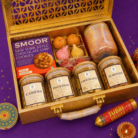 Open gold Diwali gift case packed with four labelled jars, a scented candle, a gold tray of modak and ladoo candles and a carton of chocolate chip cookies