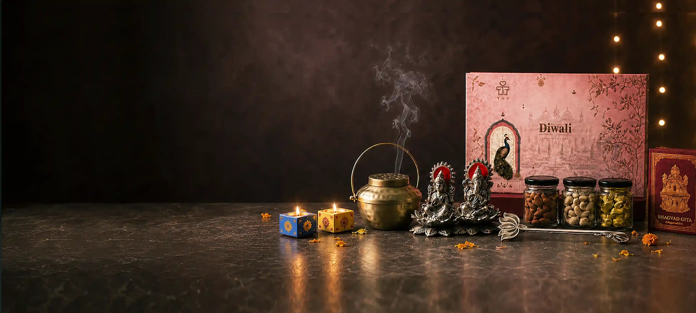 Diwali gift hamper — brass diya pot, Lakshmi and Ganesha idols, dry fruit jars and a pink Diwali gift box lit by festive lights