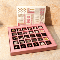 Open premium chocolate gift box with 25 assorted chocolates in a pink divided tray, block-printed lid standing behind