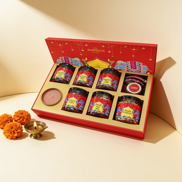 Subh Deepavali gift hamper open in the red elephant box: Maharaja Masala Chai, Kashmiri Kahwa Chai, Signature Bold Coffee, chocolates, Diwali nut mix, mouth freshener, ghee and a scented candle, with a brass diya and marigolds
